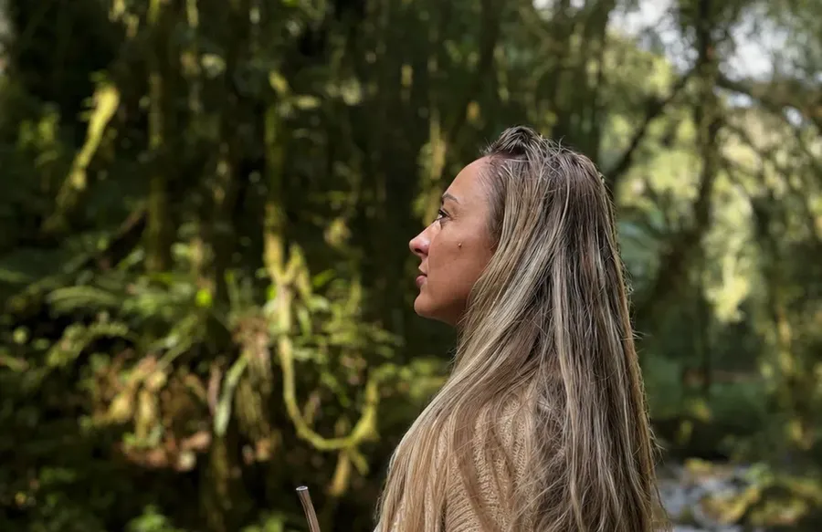 Fabiele Ullmann Schons de perfil, em meio à mata, olhando as árvores